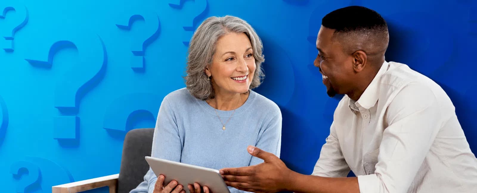 Senior woman and young man discussing and smiling while holding a digital tablet against a blue question mark background