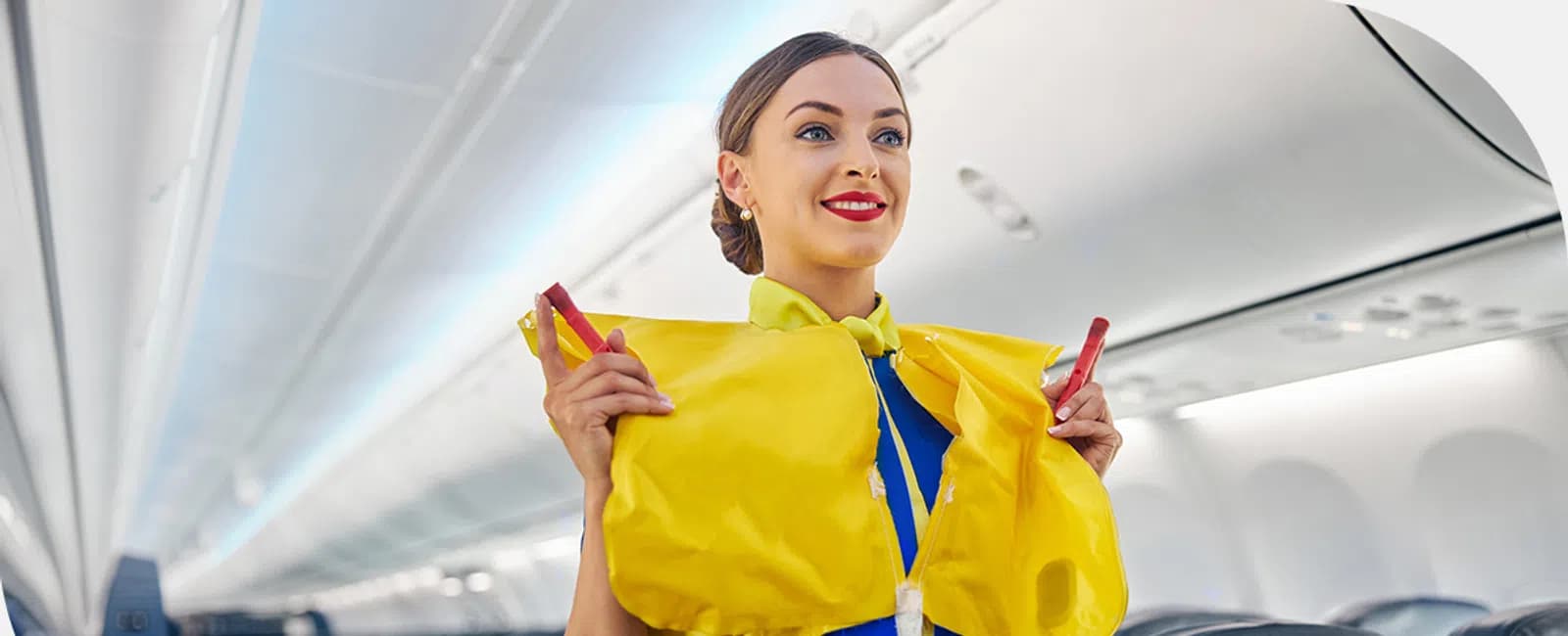 Flight attendant demonstrating the use of a yellow life vest inside an airplane cabin.