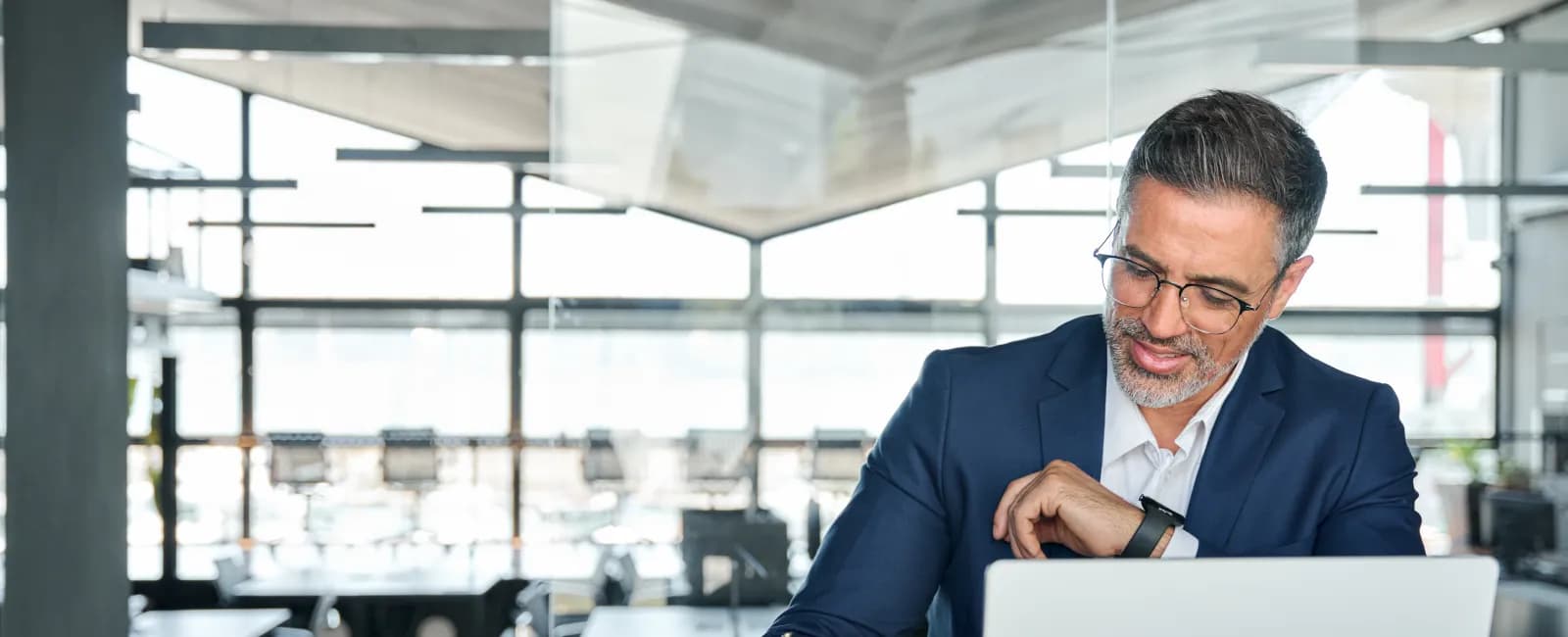 Man in blue suit working on laptop and writing notes in a modern bright office space.
