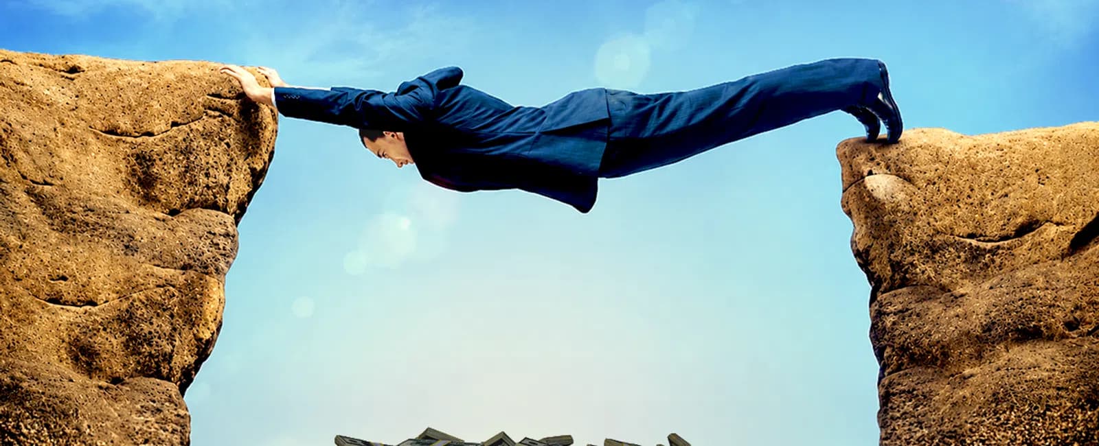 Businessman in suit bridging a gap between cliffs with money below, symbolizing risk and opportunity.