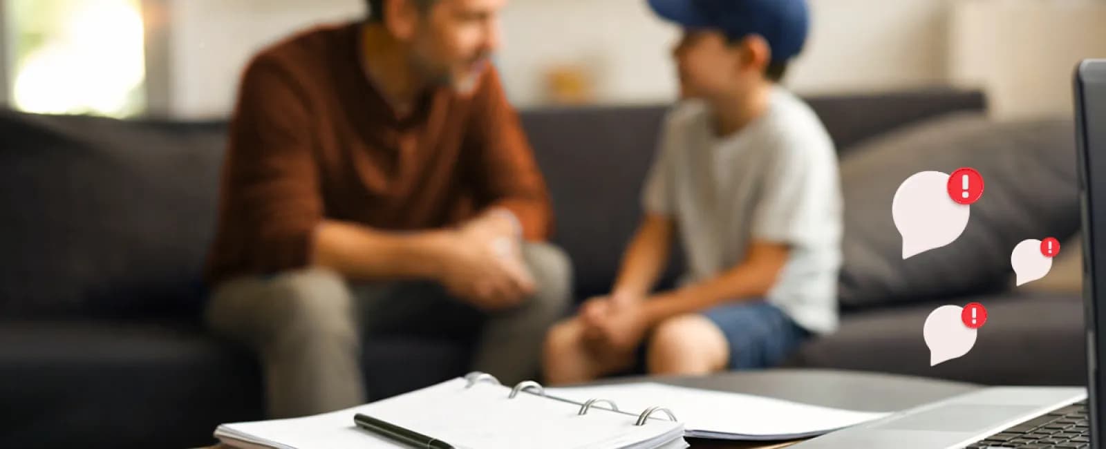 Father and son talking on couch with laptop, notebook, and smartphone on table in foreground