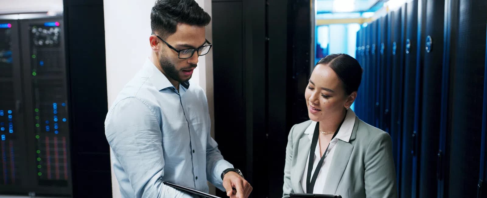 IT professionals discussing data with digital tablets in a server room filled with racks and equipment.
