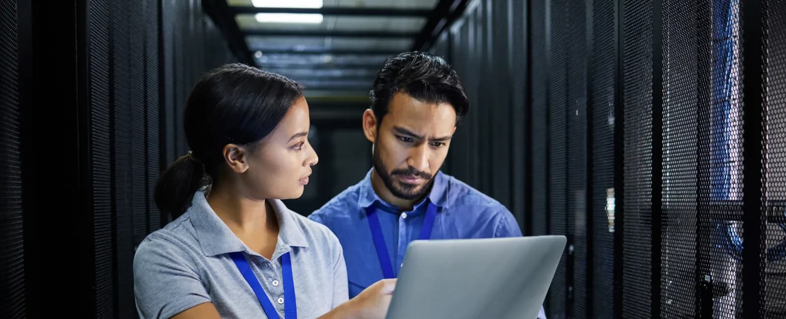Two IT professionals discussing data on a laptop inside a data center with server racks around them.